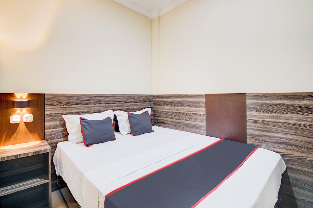 Una cama bien tendida con una colcha blanca y roja, dos almohadas y un cabecero de madera.