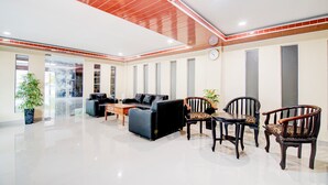 A spacious lobby with a black leather sofa, wooden chairs, a wooden table, and a potted plant.
