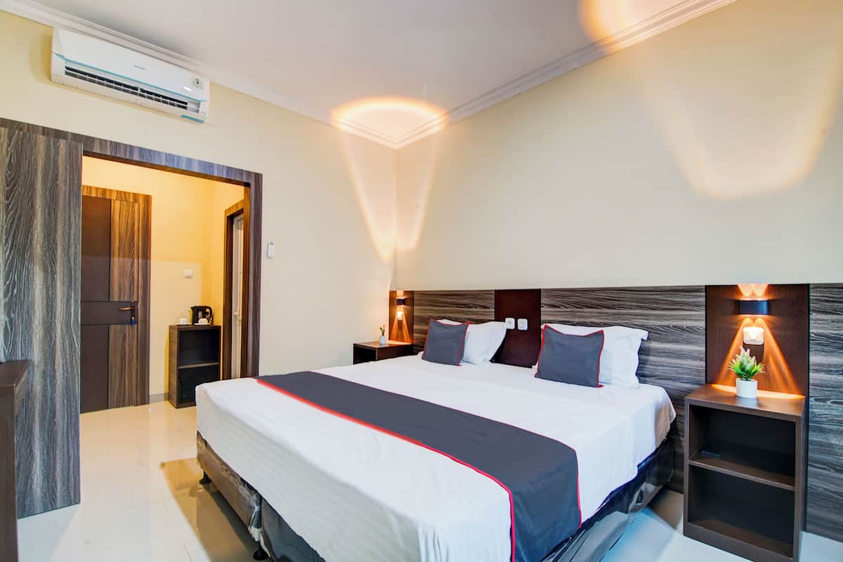 Una habitación de hotel moderna con una cama grande, mesitas de noche, un equipo de aire acondicionado y una puerta que da a otra habitación.