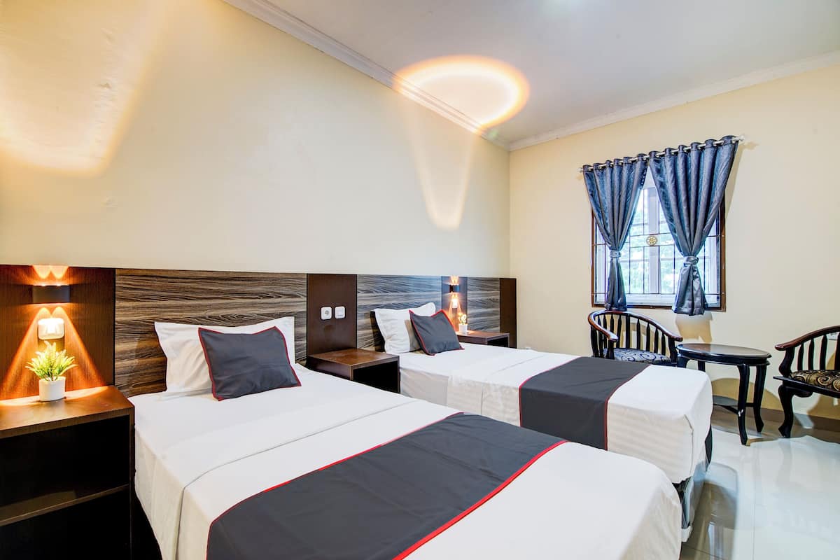Habitación de hotel con dos camas, una mesita pequeña y una silla.