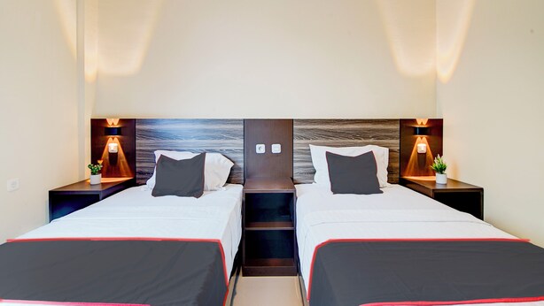 A hotel room with two beds, each with a wooden headboard, bedside lamps, and a small plant on the nightstand.