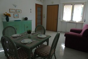 Un coin repas avec une table dressée pour quatre personnes, entourée de chaises, d’un meuble vert et d’un canapé violet.