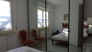 A bedroom with a bed, a chair, a mirror, and a window.