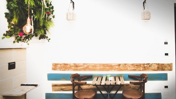 Un comedor con una mesa y sillas de madera, un lámpara colgante y una planta en la pared.