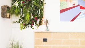 Una habitación con pared de ladrillo, un taburete de madera, una planta en maceta y un aplique de pared.