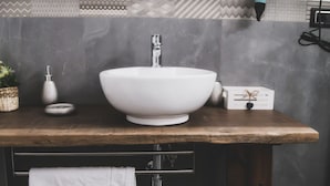 Un baño con un lavabo blanco tipo recipiente, una encimera de madera, una toalla colgada en un perchero y un salpicadero de azulejos con diseño.