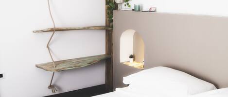 A bedroom with a bed, a hanging plant, a shelf, and a small window.