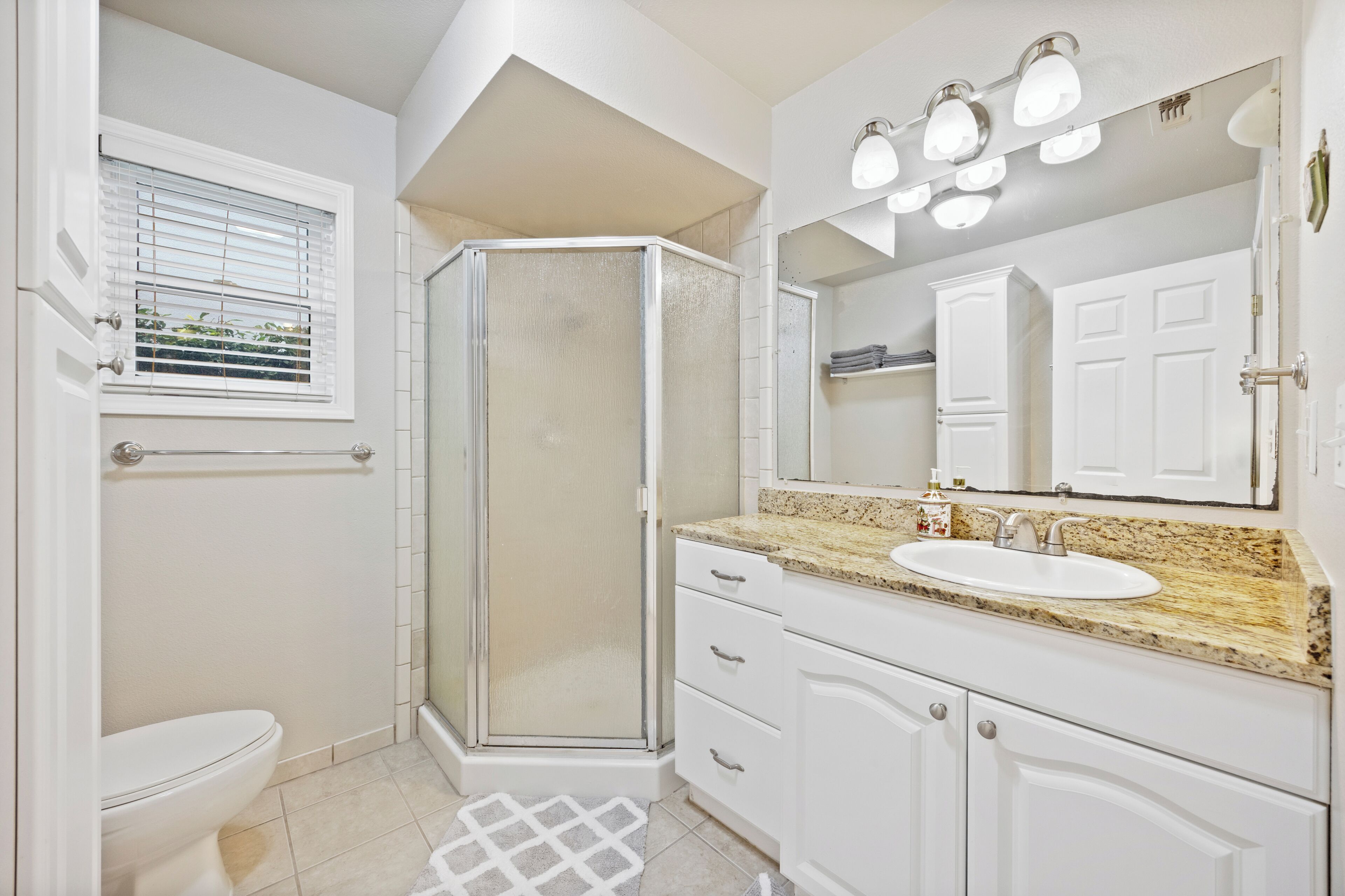 A bathroom with a toilet, shower, sink, and vanity.
