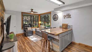 A modern kitchen with a central island, grey cabinets, and a large window providing a view of the outdoors.
