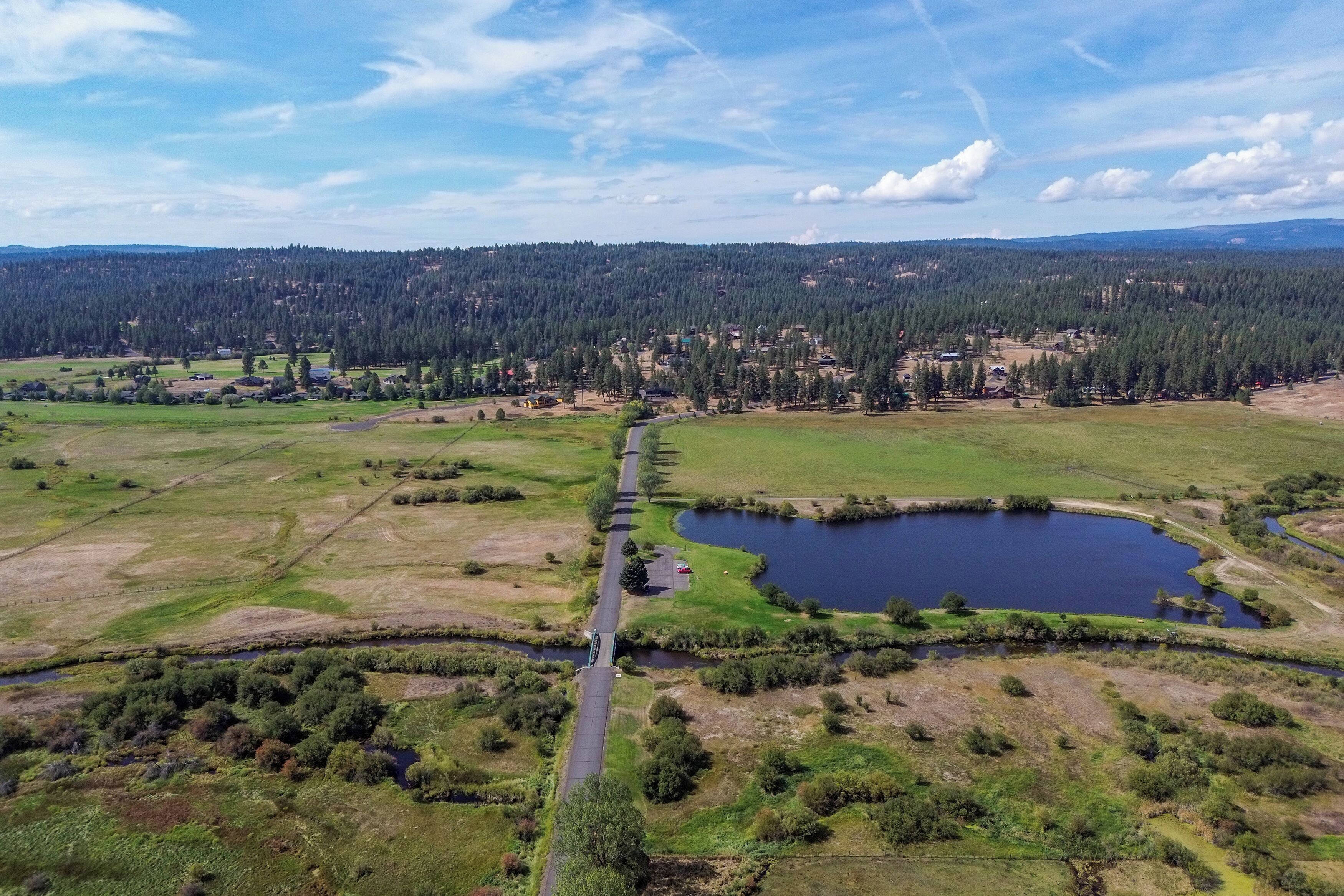 An aerial view of a rural landscape with a road, a small lake, and a forested hill in the background.