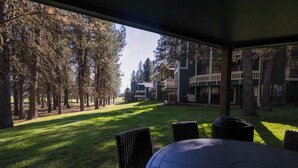 A covered outdoor area with a table and chairs, surrounded by trees and buildings in the background.