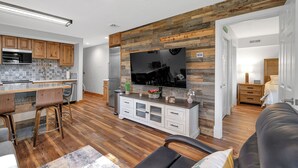 A modern kitchen with wooden cabinets, a large TV, and a dining area with bar stools.