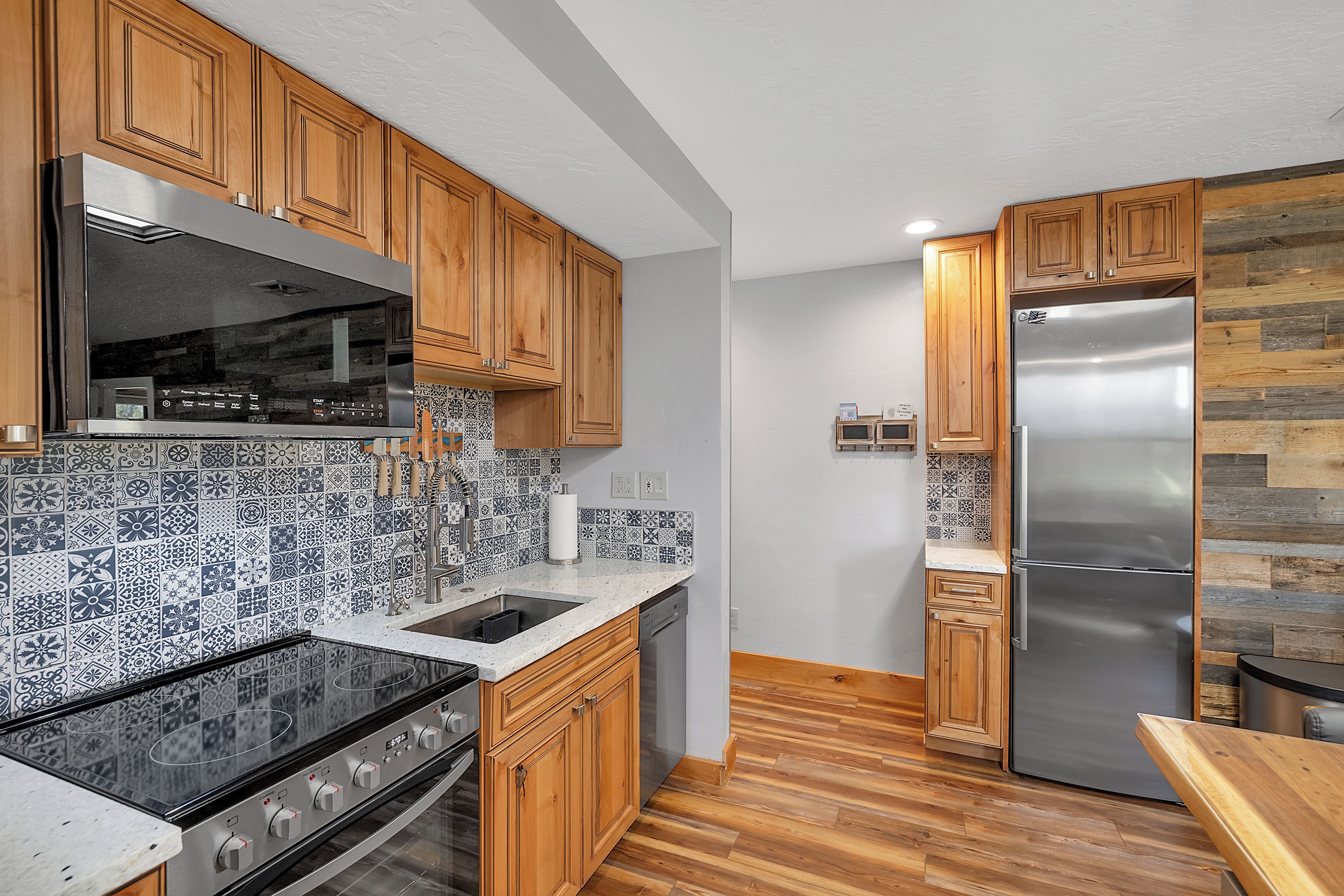 Eine moderne Küche mit Holzausstattung, einem Edelstahlkühlschrank, einem Einbauofen und einer Muster-Spritzschutzwand.