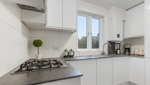A modern kitchen with white cabinetry, a gas stove, a sink, and a window providing natural light. - Modern 5-Bedroom Fulham Flat - Sleeps 12 (London)