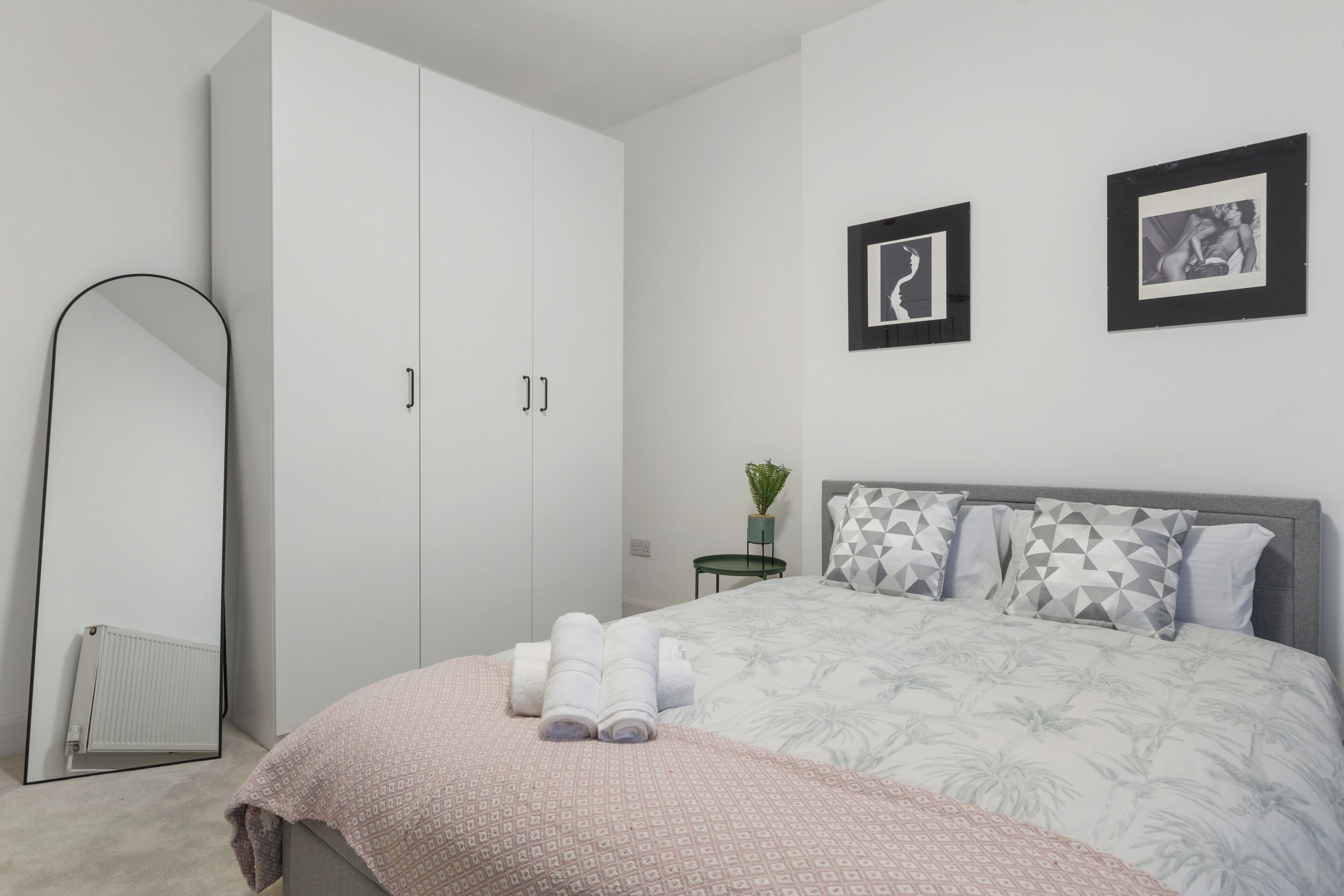 Een slaapkamer met een grote kledingkast, een bed met beddengoed met een patroon, en twee ingelijste foto’s aan de muur.