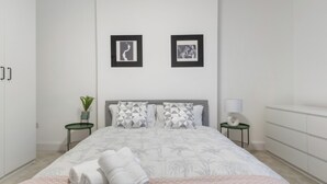 A modern bedroom with a large bed, two framed pictures on the wall, a bedside table with a lamp, and a green plant. - Modern 5-Bedroom Fulham Flat - Sleeps 12 (London)