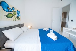 Une chambre d’hôtel avec un lit, un tableau, un bureau et une salle de bain visible à travers une porte ouverte.