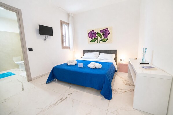 A bedroom with a bed, a flat-screen TV, a painting, a bedside table, and a nightstand.
