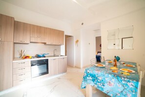 A modern kitchen with wooden cabinets, a built-in oven, and a dining area with a floral tablecloth.