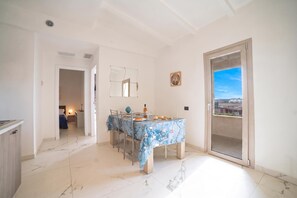 A dining area with a table set for two, a sliding glass door to a balcony, and a view of the cityscape. - Pino 3 - 3 bedrooms Near The Sea, Nardò, Italy (Nardò)