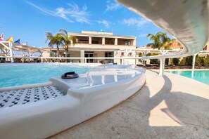 A pool area with a lounge chair, a poolside chair, and a building with multiple balconies in the background.