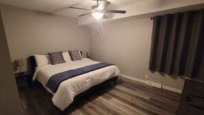 Ein Schlafzimmer mit einem Bett, einem Deckenventilator, einem Nachttisch und einem Fenster mit Vorhängen.