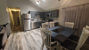 Eine moderne Küche mit Edelstahlgeräten, ein Essbereich mit schwarzem Tisch und weißen Stühlen sowie ein Deckenventilator.