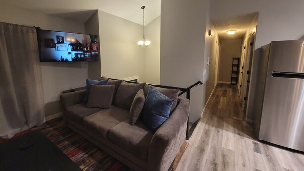 Ein Wohnzimmer mit einer Couch, einem Flachbildfernseher, einem gemusterten Teppich und einer Küchenzeile mit einem Kühlschrank.