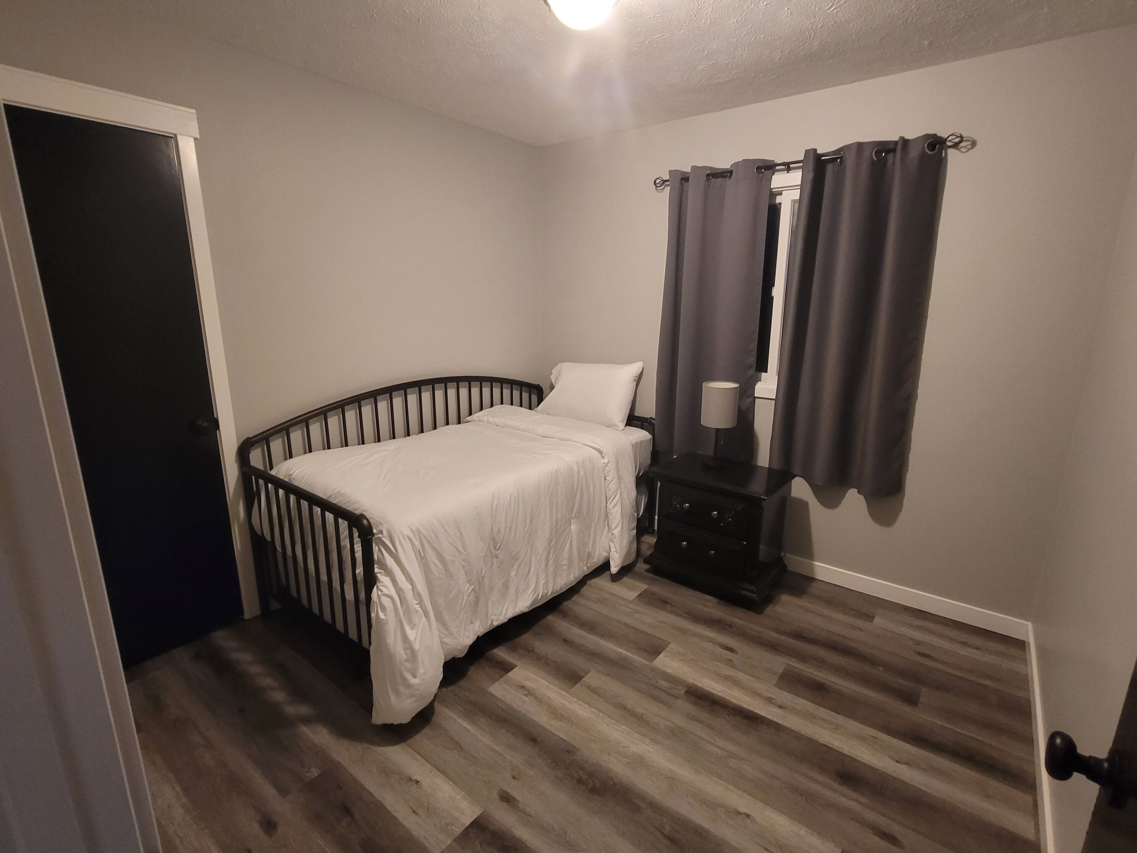 Une chambre à coucher avec un lit, une table de chevet, une lampe et une porte.