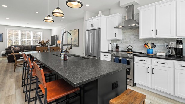 Una cocina moderna con armarios blancos, una isla grande con taburetes de bar, electrodomésticos de acero inoxidable e iluminación colgante.