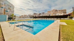 Una piscina con una scala in metallo, circondata da una zona pavimentata e un prato.