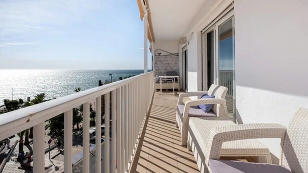 Un balcone con mobili in vimini bianco, vista sul mare e pavimento piastrellato.