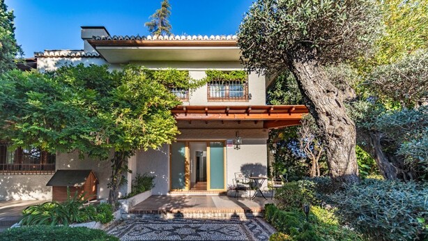 A modern house with a tiled patio, surrounded by lush greenery and a large tree. - Luxury Villa! Pool, Garden, and Jacuzzi. Granada (Albolote)