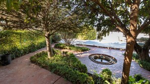 A paved pathway with a circular water feature, surrounded by lush greenery and trees. - Luxury Villa! Pool, Garden, and Jacuzzi. Granada (Albolote)