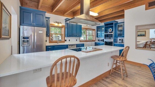 A modern kitchen with wooden beams, blue cabinets, a stainless steel refrigerator, and a large island with bar stools. - Large Family Home, Pool, Pet Friendly and Steps from the Beach (Jekyll Island)