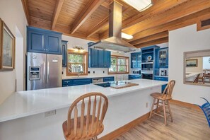 A modern kitchen with wooden beams, blue cabinets, a stainless steel refrigerator, and a large island with bar stools. - Large Family Home, Pool, Pet Friendly and Steps from the Beach (Jekyll Island)