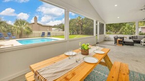 A spacious patio with a wooden table set for dining, overlooking a swimming pool and a backyard. - Large Family Home, Pool, Pet Friendly and Steps from the Beach (Jekyll Island)