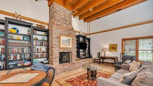 A spacious living room with a fireplace, bookshelves, a dining table, and a comfortable seating area. - Large Family Home, Pool, Pet Friendly and Steps from the Beach (Jekyll Island)