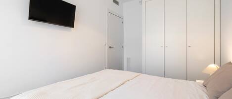 Une chambre à coucher avec un lit, un téléviseur fixé au mur, une armoire et une lampe.