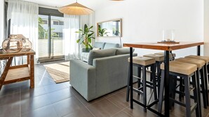 Una sala de estar moderna con un sofá gris, una mesa de comedor de madera con taburetes tipo bar y dos grandes lámparas colgantes tejidas.