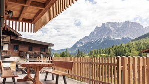 Eine Holzdielen-Terrasse mit Tisch und Bänken, mit Blick auf eine Berglandschaft.