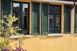 A building with multiple windows, each with green shutters, and a yellow facade.