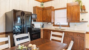 Eine Küche mit Holzausstattung, einem Kühlschrank, einem Backofen und einem Esstisch mit Stühlen.