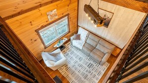 Ein Interieur einer Holzhütte mit Holzbalkendecke, einer Couch, einem Tisch und einem Fenster.