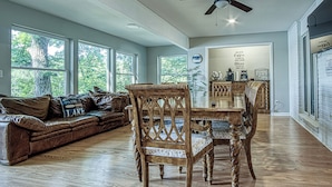 A spacious living room with a wooden floor, a brown leather couch, a wooden dining table with chairs, and a ceiling fan. - Amazing Views, Huge Game Room, Dock, Deck, Sleeps 16, Free Kayaks! (Hot Springs Village)