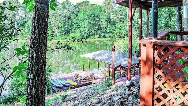 A wooden deck with a covered seating area overlooking a lake, surrounded by trees. - Amazing Views, Huge Game Room, Dock, Deck, Sleeps 16, Free Kayaks! (Hot Springs Village)