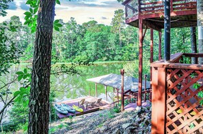 Une terrasse en bois dotée d’un espace salon couvert, donnant sur un lac et entourée d’arbres.