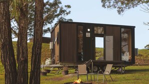 Une petite cabane en bois avec un foyer et des chaises à l’extérieur.