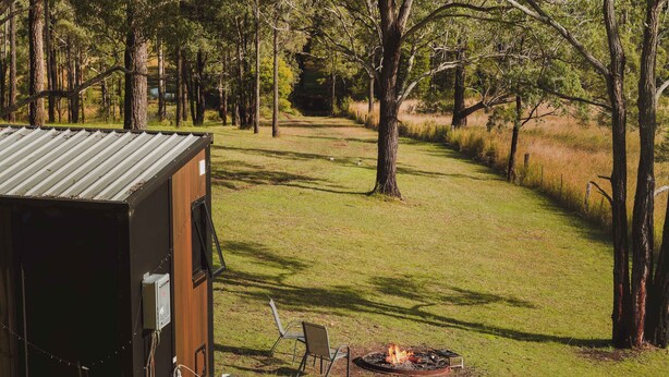 Un terrain de camping avec une cabane dont le toit est en métal, un foyer et une chaise.