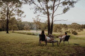 Two people seated at a table with a fire in the background, surrounded by trees and open grassland. - One-Gaea by Tiny Away (Rainbow Flat)